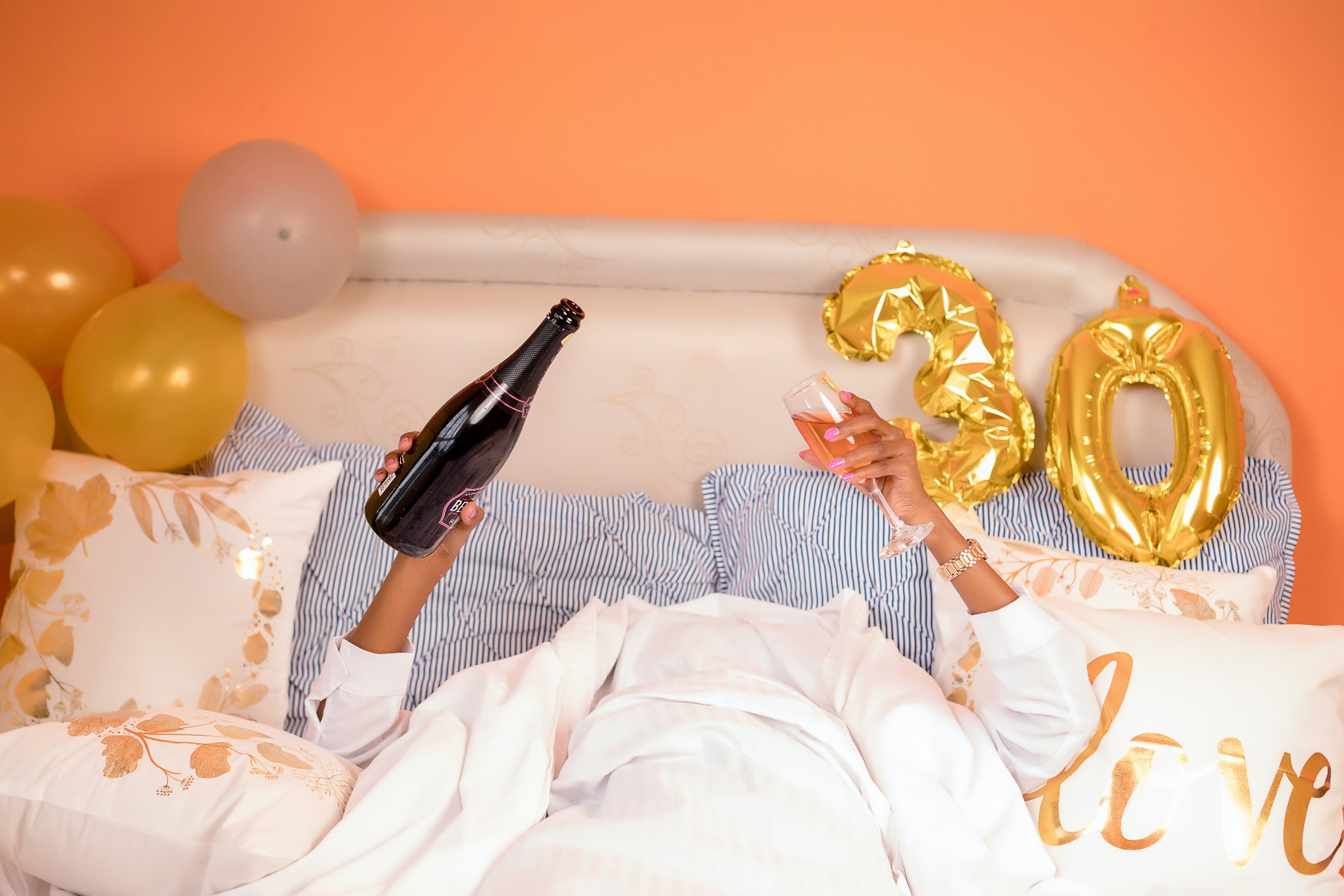 Femme dans son lit le lendemain de ses 30 ans, coupe de champagne et bouteille en main Femme dans son lit le lendemain de ses 30 ans, coupe de champagne et bouteille en main